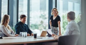 A group of business people sitting around a conference table and a business woman standing at the end presenting a training