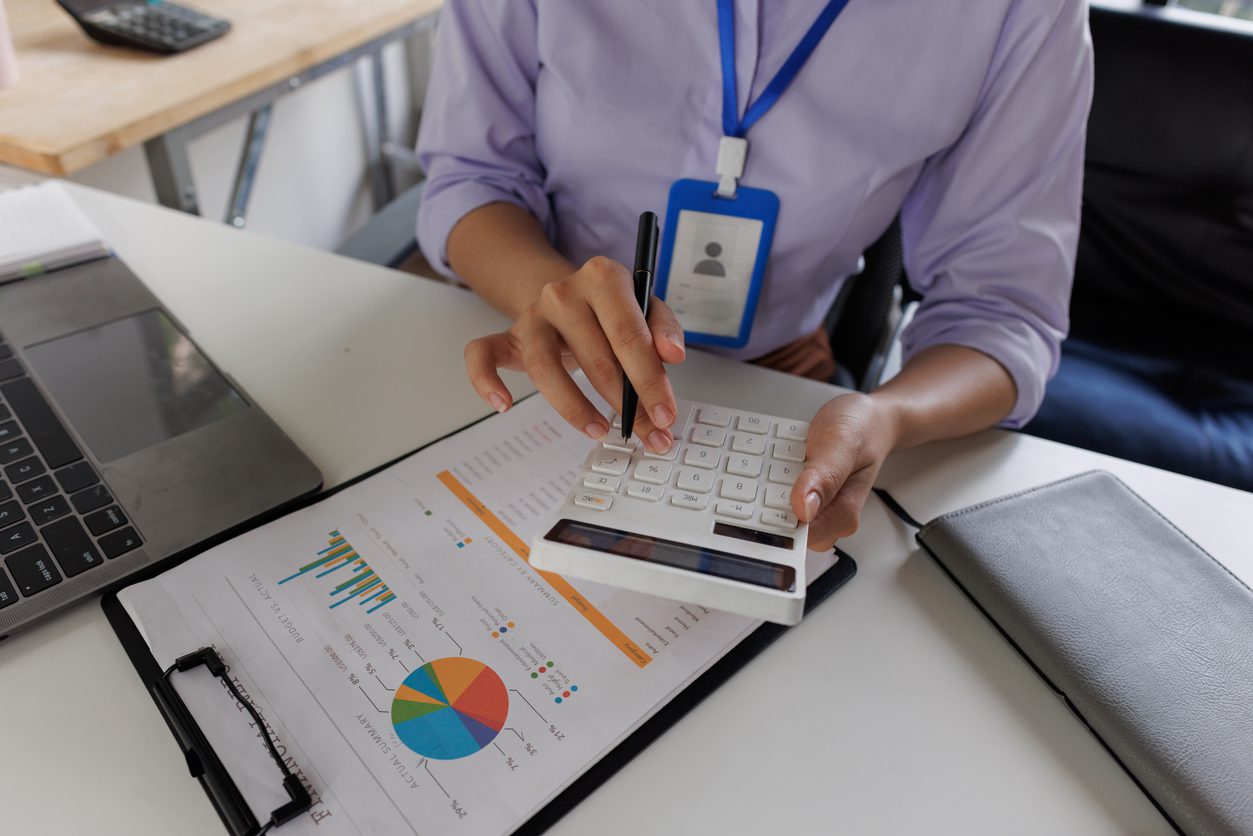 Close up of business woman or accountant hand holding pen working on calculator to calculate business data, accountancy document and laptop computer at office, business concept