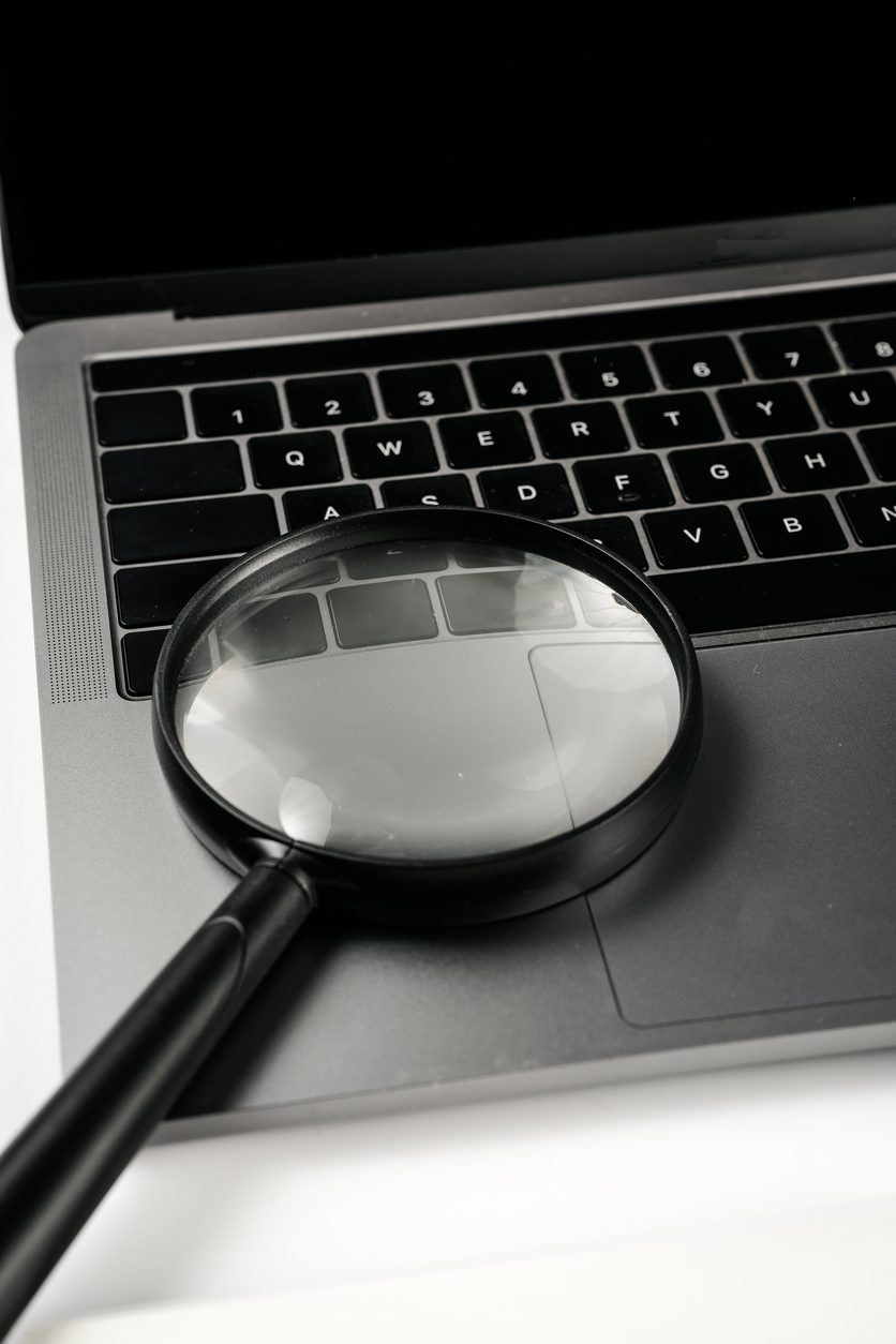 Computer and magnifying glass on white background board