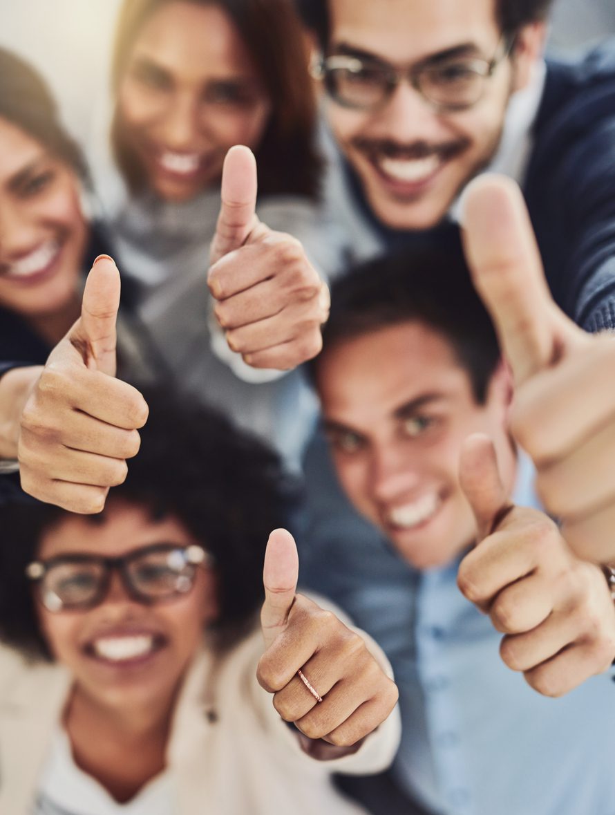 Portrait of a group of cheerful businesspeople showing thumbs up in an office during the day
