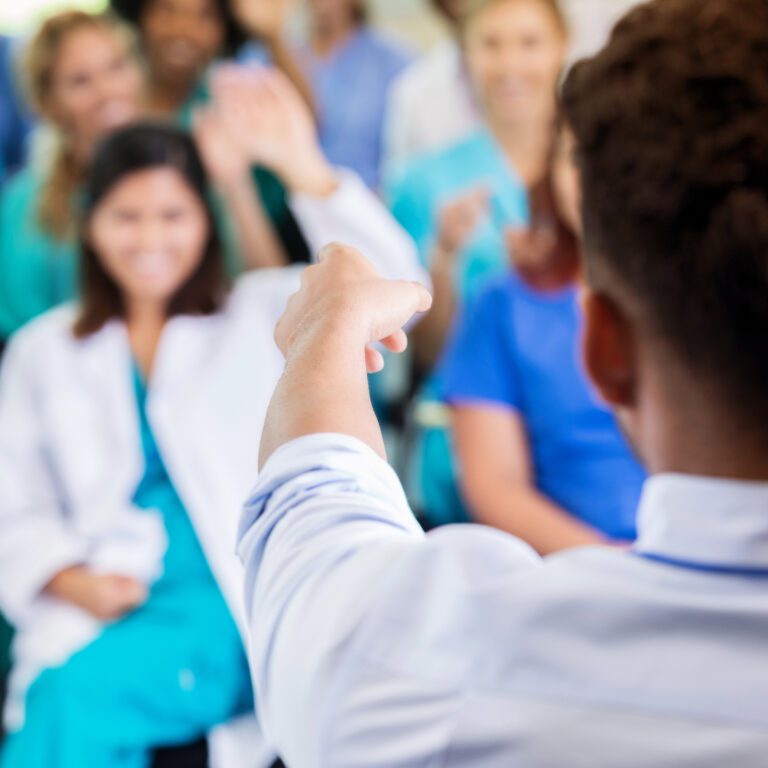 Unrecognizable male doctor or medical school professor points to someone in classroom or medical conference to ask a question.